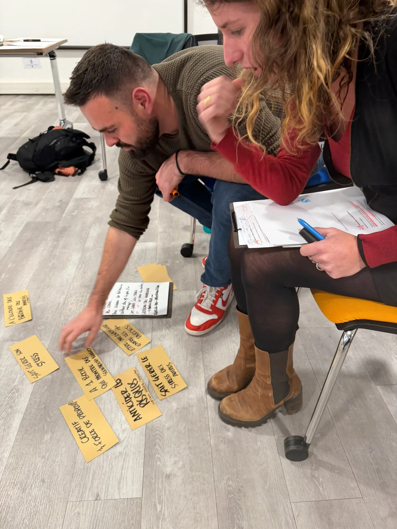 Nicolas Verdot et une participante penchés sur des cartes jaunes posées au sol, qu’ils trient ensemble